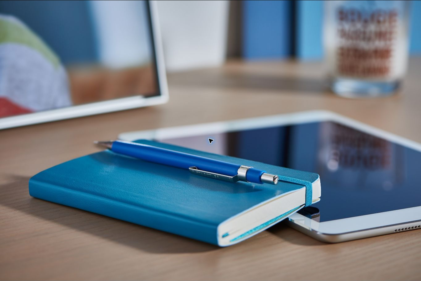 Notebook, pen, tablet, and computer arranged on a creative workspace