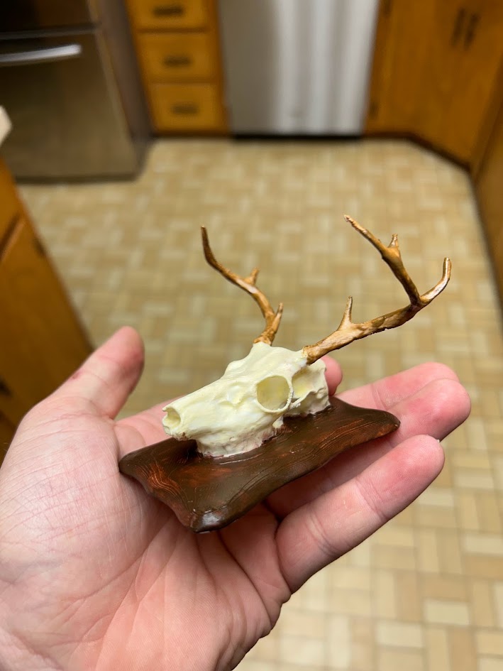 Miniature 3D-printed deer skull with antlers on a wood-look display base
