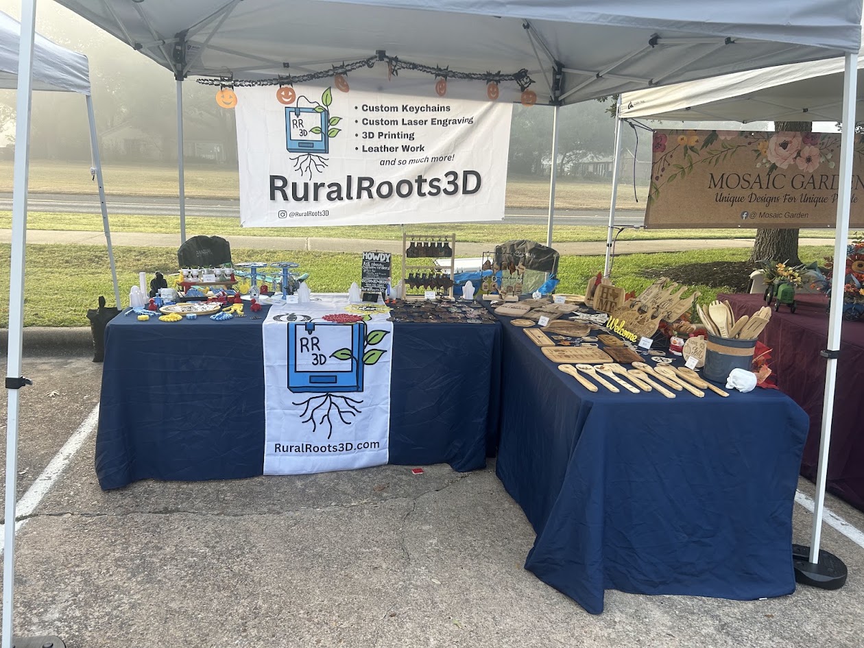 RuralRoots3D market booth with blue tablecloths, products, and branded banners